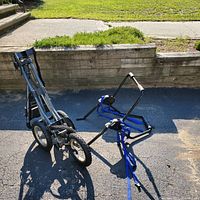Photo showing a foldable golf cart and a foldable bike rack on pavement outdoors in sunlight.