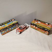 Two 1/24 scale NASCAR diecast cars placed on white surface, one boxed and one out of box with Halloween Peanuts graphics.