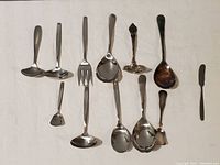 Full view of all 10 flatware items arranged on a white surface showing different types of spoons and a fork with mixed finishes and some oxidation.