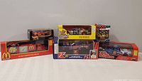 Wide shot showing six unopened Nascar diecast cars in original packaging, various colors and sponsors visible