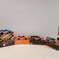 Five 1/24 scale NASCAR diecast cars displayed on their original boxes with distinct colors and sponsor logos visible.