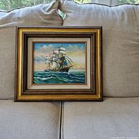 Frontal view of the framed oil painting, showing the ship at sea with a gold-tone multi-layer wooden frame and linen matting.