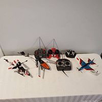 Full view of all R/C helicopters, plane, and controllers arranged on a white surface.
