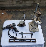 Photo showing all items together on white cloth including drill presses, electric drill, caliper, and level.