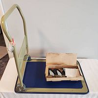 Photo showing the work cart base with a fixed beige handle and a box with wheels on top.