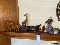 Shows entire set of wood and ceramic animal figurines on a wooden mantel against a white brick wall for size and composition reference.