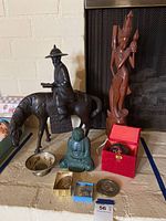 Full lot including metal man on horse statue, wood statues, Buddha figures, metal bowls, and small ornaments shown together on floor.