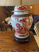 Photo of the Asian-style ceramic lamp base showing the reddish-brown traditional figures and scenes on cream ceramic, mounted on a dark wooden round base.