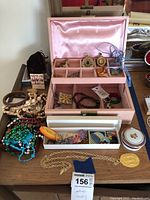 Overall view of pink jewelry box on table with assorted jewelry and exterior small drawers with beads and bracelets visible