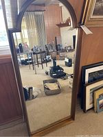 Full front view of full-size rectangular mirror with arched top and wooden frame reflecting a room interior.
