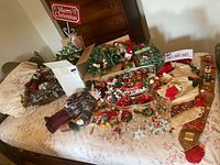 Photo of various Christmas decorations and ornaments laid out on a bed surface, capturing the full assortment including signs, garlands, stockings, and small decorations.