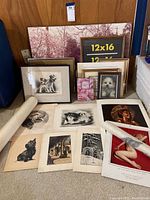 Overall view of multiple framed and rolled prints on floor including dog sketches, small dog photo, abstract print, large placeholder frame with size label, and rolled prints