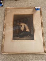 Framed print showing nude woman kneeling with long hair, draped fabric, in a gold frame with double mat.