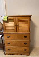 Full view of the tallboy dresser showing shutter-style double doors at top and three drawers below with metal handles, medium wood tone.