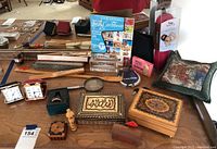 Full overview of lot showing all items on a large wooden tray, including travel clocks, fans, travel mementos, wooden boxes, a magnifying glass, a Caribbean travel guide, and a decorative pillow.