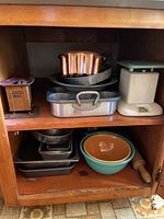 Photo showing assorted vintage metal bakeware such as cake and loaf pans, fluted mold, plastic measuring container, and ceramic mixing bowls on wooden shelves.