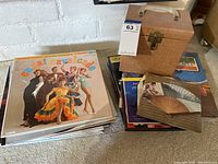 Stack of vintage vinyl records with album cover of Xavier Cugat and His Orchestra at top alongside pink textured record carrying case and hand fan.