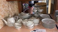 Photo of the entire violet Fontaine china set including teapot, sugar bowl (handle missing), cups, saucers, plates, serving platters, and tiered stand on a countertop.