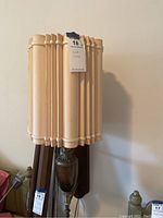 Front view of wall lamp with beige pleated lampshade and wooden backplate.