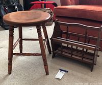 Wooden stool and wooden magazine rack side by side on carpet with couch and bags in background
