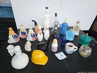 Front view of all Avon bottles on black surface showing variety including milk glass, patriotic women, bowling pins, dog shapes, golf club bottle, yellow hard hat, blue stoneware bottle, and decorative jars.