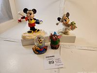 Four Disney figurines placed together featuring Mickey Mouse in beach and holiday themes, Pluto inside a mini snow globe, and Gus from Cinderella.