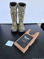 Pair of Bogs boots with leaf pattern standing upright next to the Hoglund's Boot Jack on a black surface.