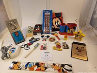 Overview of Disney office supplies lot showing rulers, pencils, Mickey computer mouse, keychains, pen holders, and other items arranged on white surface.