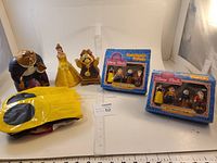 Three Beauty and the Beast puppets (Beast, Belle, Cogsworth) next to two boxed Disney Town Square Friends sets (Snow White and 3 Dwarfs), plus vintage inflatable Mickey Mouse pool toy folded on table.