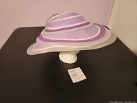 Front-left side angle view showing the large wide brim with layered purple, lavender, and white ribbon detail.