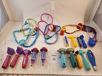 Full view of the medical play toy items arranged on white surface showing multiple stethoscopes, handheld medical devices, and syringes.