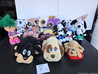 Full lot of plush toys featuring Littlest Pet Shop, Pound Puppy, Snoopy, and Troll doll arranged on a table against a white wall.