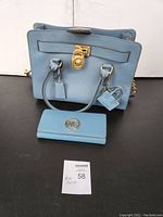 Michael Kors light blue purse with matching wallet shown together on dark surface
