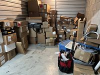 Storage unit interior with stacked cardboard boxes, plastic bins and red tool bag