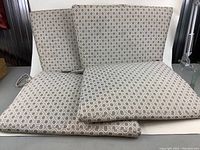 Four dining chair cushions stacked together showing a repetitive green and white geometric pattern of squares and circles