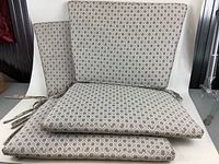 Four dining chair cushions stacked, showing geometric patterned fabric and ties.