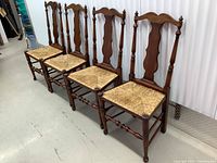 Four solid wood dining chairs with woven seats, arranged in a row showing minor wear on legs and seats.