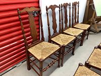 Photo showing 4 solid wood dining chairs with woven seats in a row against a red storage unit door.