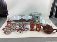 Full lot view including bowls, spoons, teapots, lidded containers, planter and clown figurine.