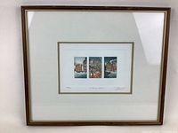 Full view of framed etching artwork showing three small colored winter urban scenes in a wooden frame with white matting and gold trim.