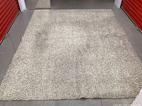 Full view of grey shag area rug laid flat on a floor in a storage unit, showing overall size and pile texture.