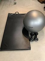 Black exercise mat laid flat on floor, showing carrying handle and surface condition.