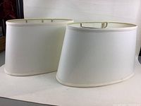 Two oval cream-colored lamp shades together, showing their shape and exterior fabric.