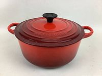 Le Creuset round cast iron pot with lid, showing front and side handles and red gradient coloring.