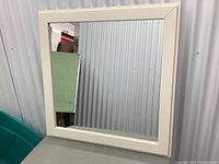 Front view of square wall mounted mirror with white wide wooden frame. Clear reflective glass, mitered corners on frame visible.