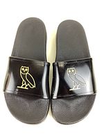 Top-down view of black OVO sliders showing gold owl logo on straps