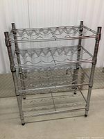 Front view of the stainless steel wire wine rack showing four tiers of wave-shaped bottle holders and adjustable pole sections.