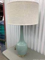 Full view of the aquamarine ceramic table lamp with white textured fabric drum lampshade on top, approx. 27 inches tall.