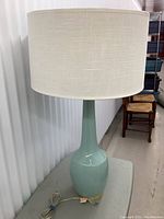 Full view of the aquamarine glazed ceramic lamp with brass base and white drum shade.
