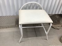 Front angled view of white vinyl stool showing padded seat, backrest, and metal frame.